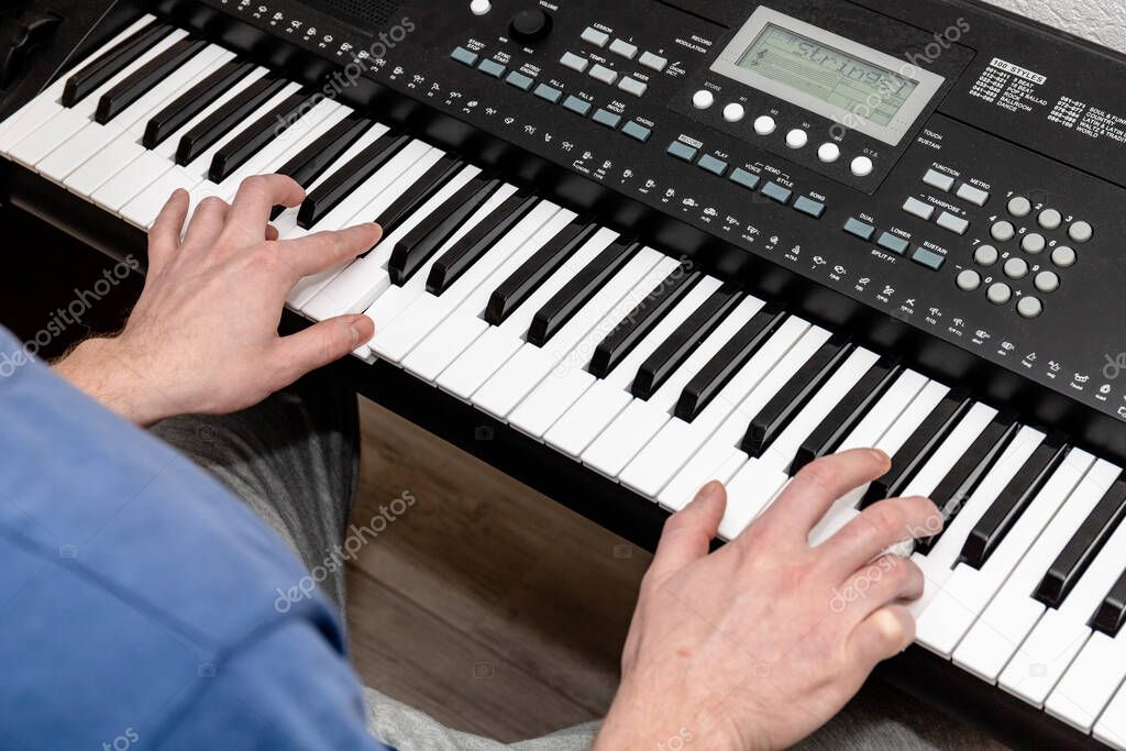hands of a pianist man playing a synthesizer in a bright home studio, top view