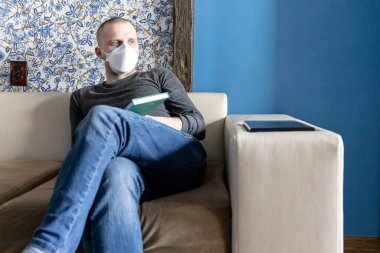 FP1 solunum cihazıyla sıkılmış genç bir adam Coronavirus covid-19 karantinası sırasında dairesinde kendini izole ediyor.