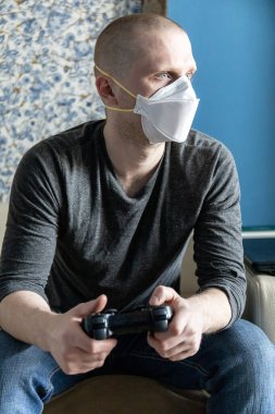 Coronavirus covid-19 salgını sırasında evinde karantinada solunum cihazı olan genç bir adam oyun konsolu oynuyor.