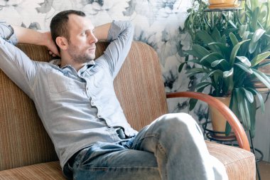 Elleri başının arkasında kanepede dinlenen genç bir adam.