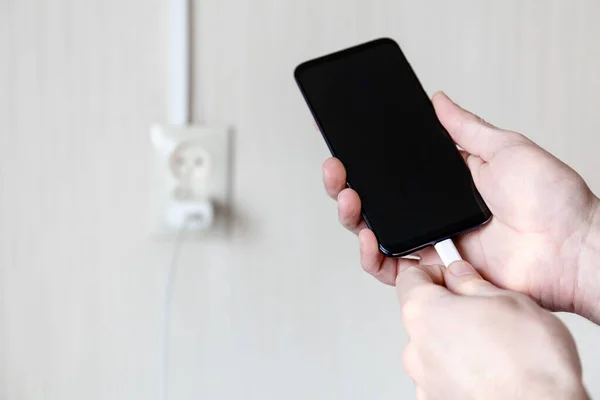 smartphone in hand on a charge on the background of the outlet