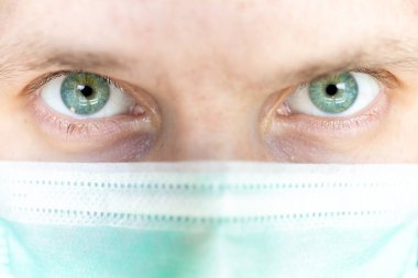 Tıbbi maskeli yeşil gözlü bir adamın süper yakın çekimi.