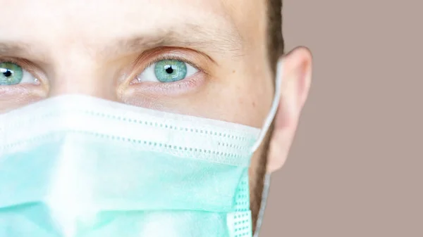 super close-up of a man\'s face with green eyes in a medical mask, copy space