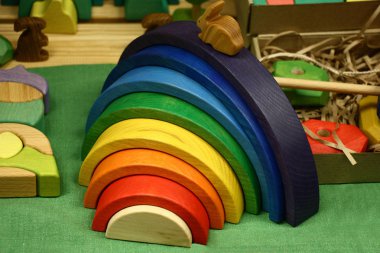 Various wooden toys lie on a table. In the centre there is a cheerful rainbow. clipart