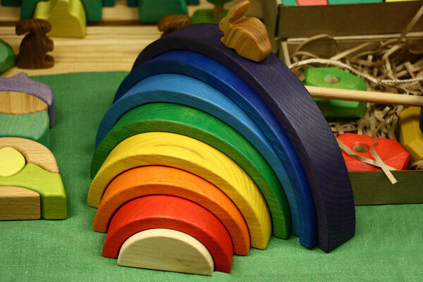 Various wooden toys lie on a table. In the centre there is a cheerful rainbow.
