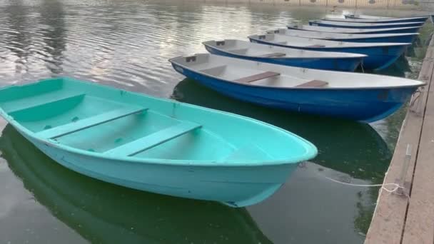 Блакитні і сині човни знаходяться на пірсі, на озері, вітер рухає їх. Його трохи дощить . — стокове відео