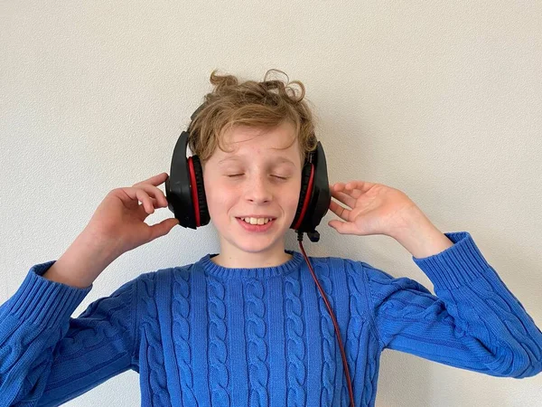 Młody mężczyzna w niebieskiej kurtce słucha muzyki, z dużymi słuchawkami na głowie. — Zdjęcie stockowe