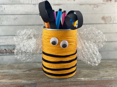 Geri dönüşümlü teneke kutudan çıkan plastik gözlü komik arı. Kalemler için ayağa kalkın.