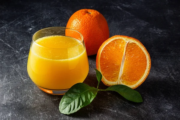 Glas Met Vers Sinaasappelsap Sinaasappels Groene Bladeren Een Donkere Achtergrond — Stockfoto