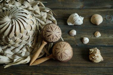 Tatil hatıraları. Palmiye yapraklarından şapka ve marakalar ve kahverengi ahşap arka planda deniz kabukları.