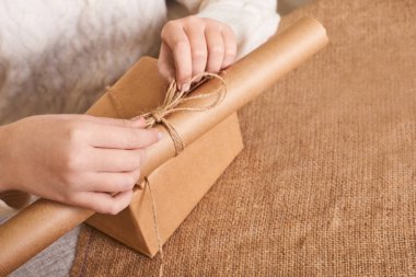 Beyaz örgü süveter paketleme kutusundaki beyaz kadın. Ellere odaklan. El işi ambalaj kağıdı ve doğal sicim. Geri dönüşüm malzemesi. Mutlu bayramlar, sürpriz. Boks günü için hediyeler. Teslimat servisi.