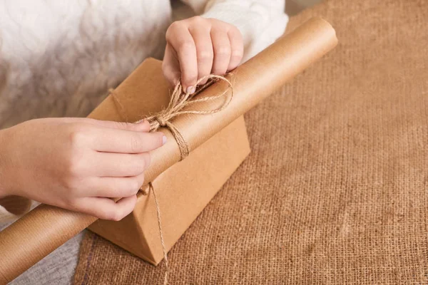 Caucasian woman in white knitted sweater packaging box. Focus on hands. Craft wrapping paper and natural twine. Recycling material. Happy holiday present, surprise. Gifts for boxing day. Delivery serv — Stock Photo, Image