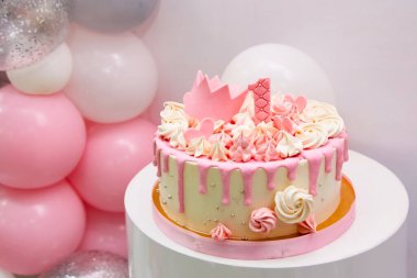 Doğum günü pastasının 1 yıllık yakın görüntüsü. Kız için dekoratif pembe pasta, prenses altın tacı ve beyaz arka planda mesaj yeri olan bir numara. Helyum balonlarıyla ilk doğum günü yıldönümü.