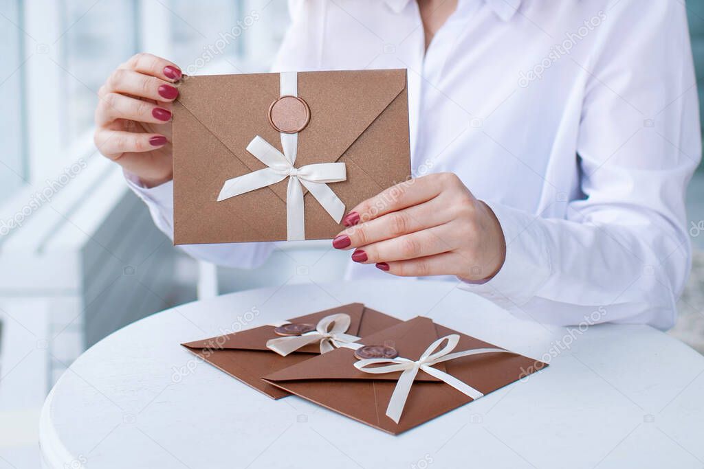 close-up photo of a female hands holding a bronze invitation envelope with a wax seal, a gift certificate, a card, a wedding invitation card