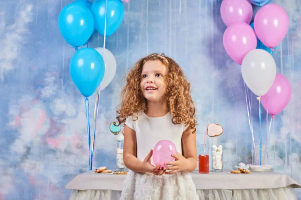 Children's funny birthday party in decorated room. Happy little girl celebrate International Children's Day. Funny child play at home