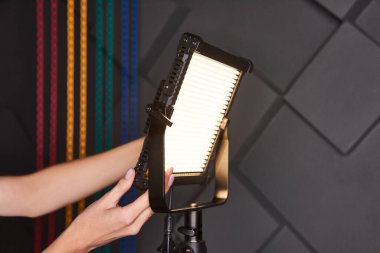 Stüdyo asistanı ayarlanabilir ışık panosundaki profesyonel video ışığını tamir etti. Fotoğraf stüdyosunda üç ayaklı lamba. Kabartmalı gri duvar arkaplanındaki fotoğraf ve video lambası. Yakın çekim görünümü