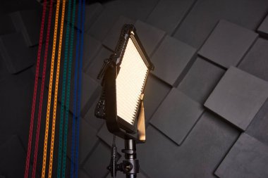 Stüdyo asistanı ayarlanabilir ışık panosundaki profesyonel video ışığını tamir etti. Fotoğraf stüdyosunda üç ayaklı lamba. Kabartmalı gri duvar arkaplanındaki fotoğraf ve video lambası. Yakın çekim görünümü