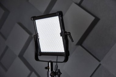 Stüdyo asistanı ayarlanabilir ışık panosundaki profesyonel video ışığını tamir etti. Fotoğraf stüdyosunda üç ayaklı lamba. Kabartmalı gri duvar arkaplanındaki fotoğraf ve video lambası. Yakın çekim görünümü