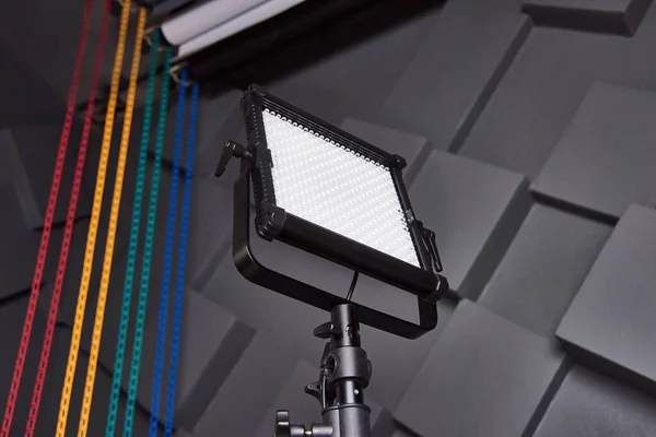 studio assistant fix professional video light on adjustable light stand. Led lamp on tripod in photo studio. Photo and video lamp on embossed grey wall background. Close-up view