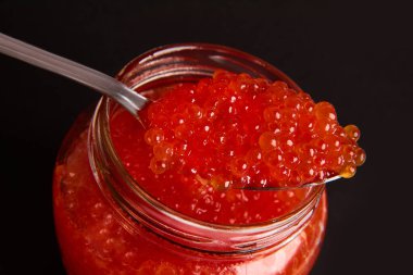 Kırmızı havyar kavanozu lüks ve siyah arka planda sağlıklı deniz yiyeceği.