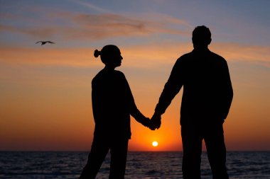 Gün batımında birbirine aşık iki insan. Silüet adam ve kadın sahilde rüya görüyorlar.