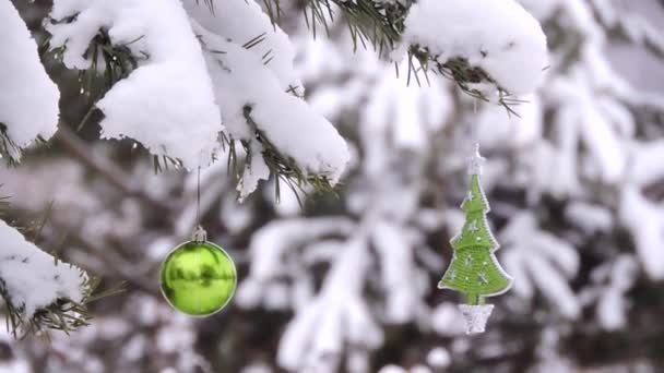 Снег зимой в лесу, ветка с рождественскими шарами, игрушки качаются на ветру — стоковое видео