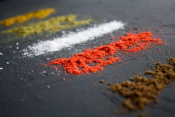 Vertical paths of different spices located on a black surface.