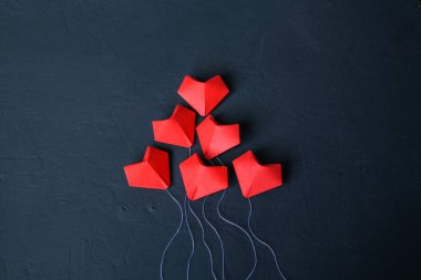 Origami kırmızı kalpleri, havada uçuşan balon şeklinde koyu mavi bir zemin üzerinde kağıttan yapılmıştır. Sevgililer Günü. Tasarım için boş alan.