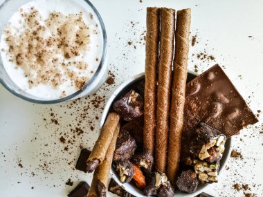 Farklı çikolatalar, çikolatalar, çikolata tüpleri masaya kakao serpiştirilmiş ve yanında bir bardak süt olan beyaz bir kasede..