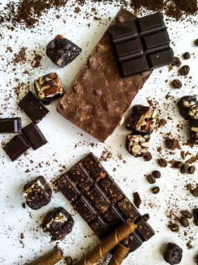 Değişik çikolata çeşitleri, beyaz bir masaya serpilmiş çikolata tüpleri kakao tozu, kahve çekirdekleri, kurutulmuş kayısılar.