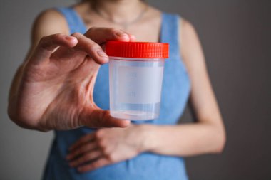 Genç hamile bir kadın önünde bir test konteynırı tutuyor..
