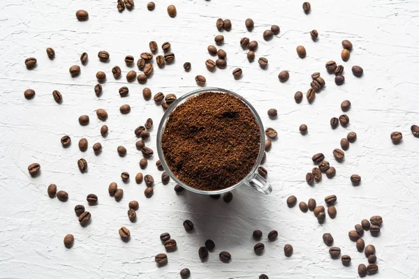 Une tasse remplie de grains de café. Les grains de café sont éparpillés sur la surface blanche de la table — Photo