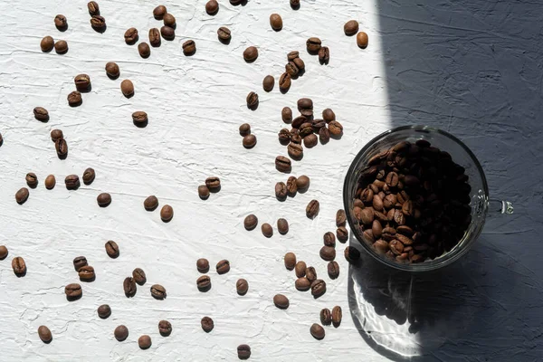 Une tasse remplie de grains de café. Les grains de café sont éparpillés sur la surface blanche de la table — Photo