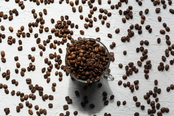 Une tasse remplie de grains de café. Les grains de café sont éparpillés sur la surface blanche de la table — Photo
