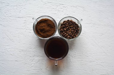 Bir sırada üç fincan kahve, kahve çekirdeği ve demlenmiş kahve.