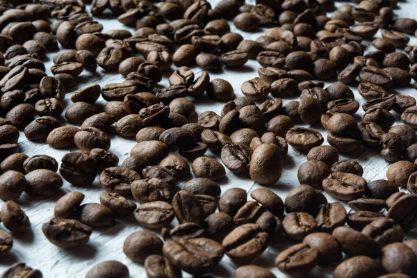 Grains de café torréfiés éparpillés sur une surface blanche — Photo