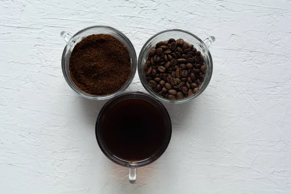 Három csésze őrölt kávé, kávébab és főtt kávé egy sorban. — Stock Fotó