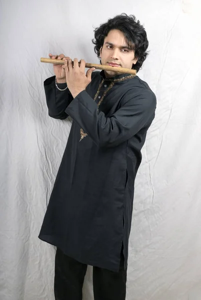 young indian male model in black kurta playing flute
