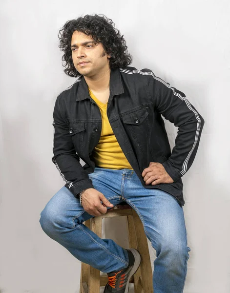 indian male model wearing yellow tshirt and blue jeans sitting pose