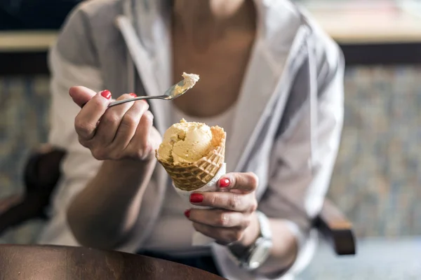 Girl holding spoon with ice cream, eating ice-cream in cafe, hands holding ice-cream