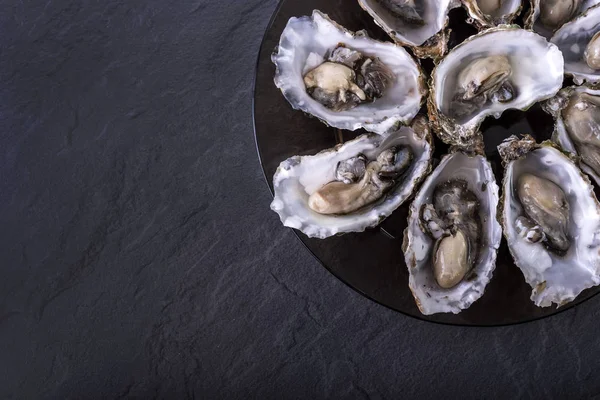 Open oysters on black plate on dark grey background.