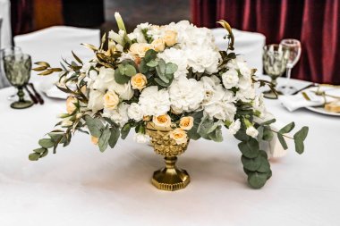 Gelinin sarı ve beyaz çiçekli buketi restoranda düğün hazırlıkları yapıyor. Restorandaki masada beyaz ve sarı şakayık ve güllerden oluşan güzel bir gelin buketi.