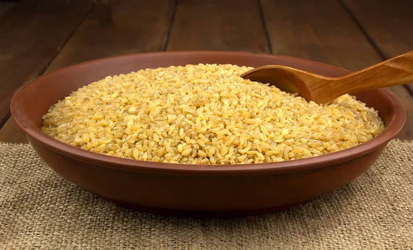 Dry bulgur wheat in a clay bowl with spoon  on the sacking — Stock Photo, Image