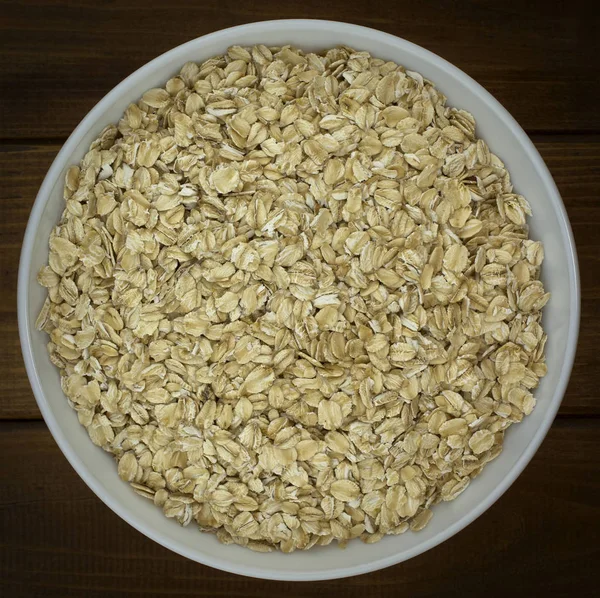 Dry oat flakes oatmeal in  bowl on wooden table — Stock Photo, Image