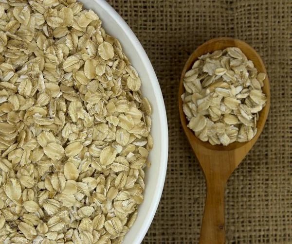 Dry oat flakes oatmeal in  bowl  on sacking with wooden spoon — Stock Photo, Image