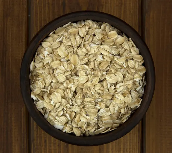 Dry oat flakes oatmeal in  bowl on wooden table — Stock Photo, Image