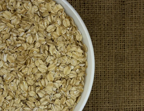 Dry oat flakes oatmeal in bowl on sacking — Stock Photo, Image