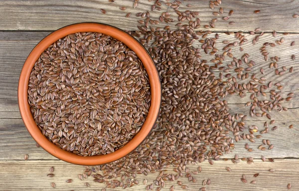 Flax seeds in bowl with scattered grains on wooden background.