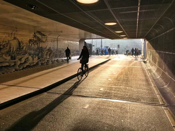 Mulher em andar de bicicleta através de um túnel iluminado para trás — Fotografia de Stock