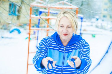 Aktif, sarışın bir kadın antrenman yapıyor ve ısınma egzersizini açık havada, karlı havada ip atlarken yapıyor.